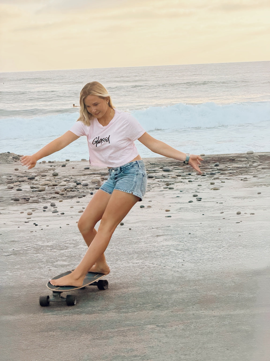 Shiloh Page wearing the pink Glassd Daily Crop Tee while carving on a skateboard by the ocean